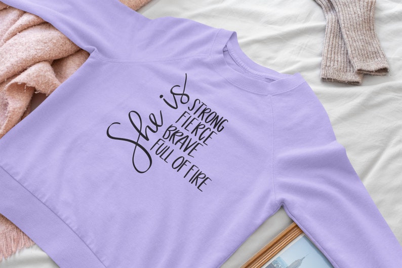 May include: A lavender sweatshirt with the text "She is strong, fierce, brave, full of fire" printed in black.