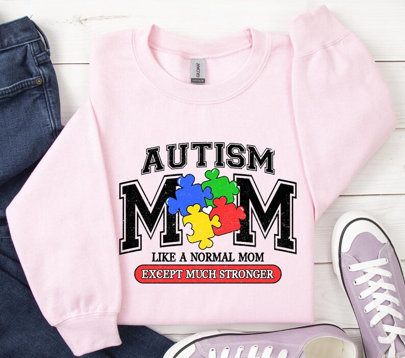May include: Pink sweatshirt with a graphic that says "Autism Mom Like a Normal Mom Except Much Stronger". The graphic features a puzzle piece design in blue, green, yellow, and red.