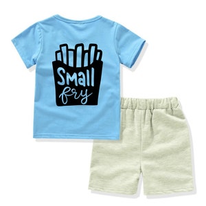 May include: A light blue t-shirt with a black graphic of french fries and the text "Small fry". The shirt is paired with beige shorts.