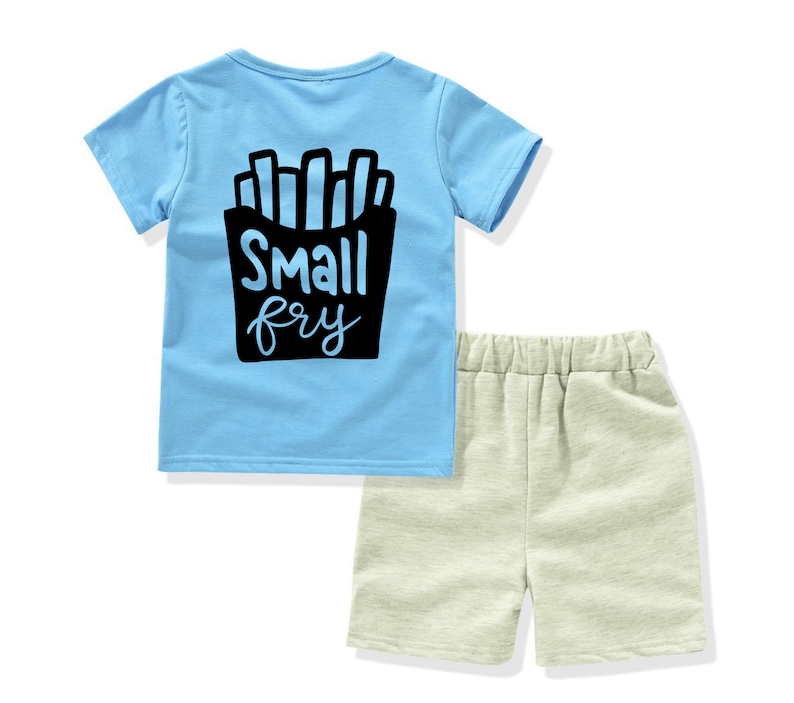 May include: A light blue t-shirt with a black graphic of french fries and the text "Small fry". The shirt is paired with beige shorts.