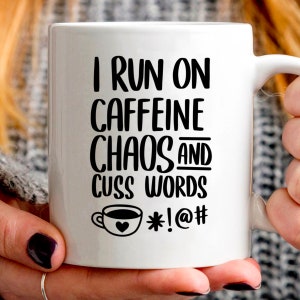 May include: White ceramic mug with black text that reads "I run on caffeine chaos and cuss words *!@#" with a small black and white illustration of a coffee cup with a heart.