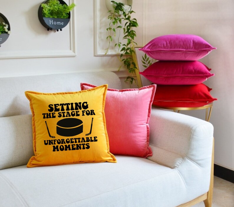 May include: A yellow throw pillow with the text "Setting the stage for unforgettable moments" and a black hockey puck graphic. The pillow is on a white couch with pink and red throw pillows.