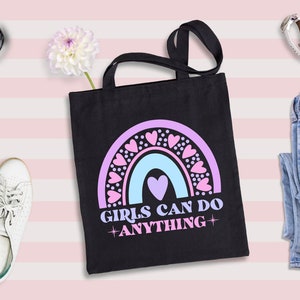 May include: Black tote bag with a rainbow design and the text "Girls Can Do Anything" in pink and blue lettering. The rainbow is decorated with pink hearts.