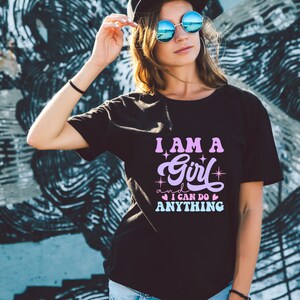 May include: A black t-shirt with a pink and purple graphic that says "I am a girl and I can do anything" with stars and hearts around the text.