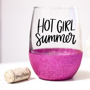 May include: A pink glitter wine glass with the text "HOT GIRL Summer" in black lettering.