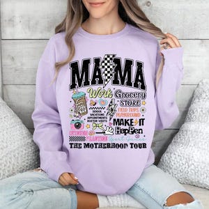 May include: Purple sweatshirt with the text "MAMA Work Grocery Store School Vacations Appointments Doctor Visits Make It Happen Kitchen Crafting Sport Games The Motherhood Tour" in black and white with colorful illustrations.