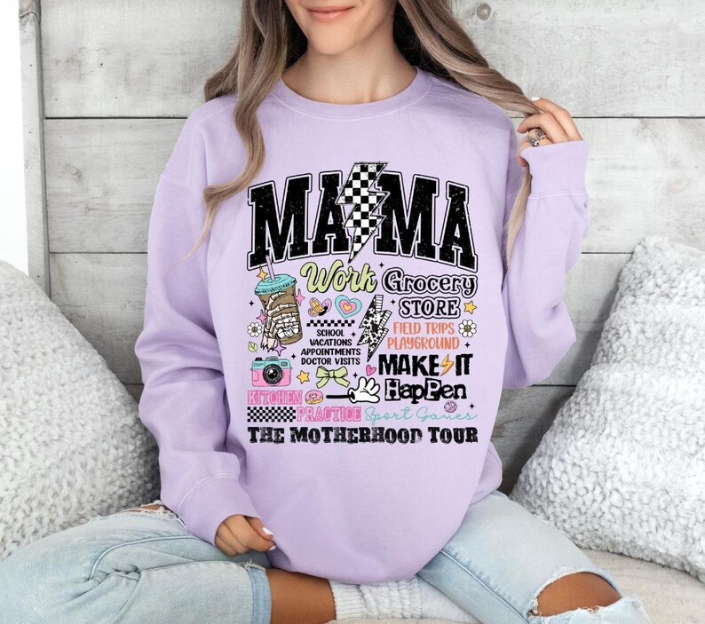 May include: Purple sweatshirt with the text "MAMA Work Grocery Store School Vacations Appointments Doctor Visits Make It Happen Kitchen Crafting Sport Games The Motherhood Tour" in black and white with colorful illustrations.
