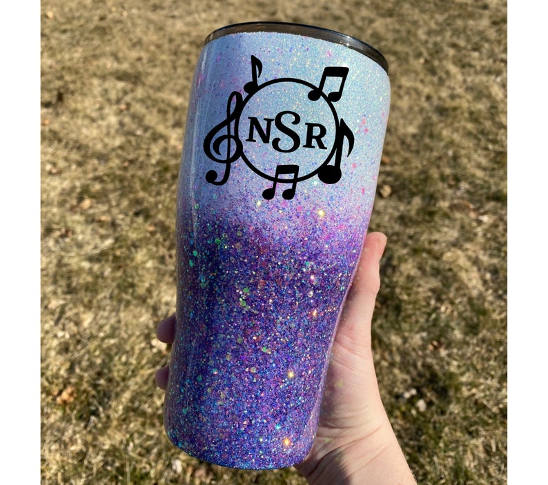 May include: A white and purple glitter tumbler with a black circle design featuring the initials "NSR" and musical notes.