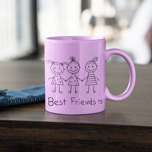 Op de afbeelding: Een lavendelkleurige keramische mok met een zwarte illustratie van drie stokpoppetjes die elkaars hand vasthouden en de tekst "Best Friends" met een hartje.