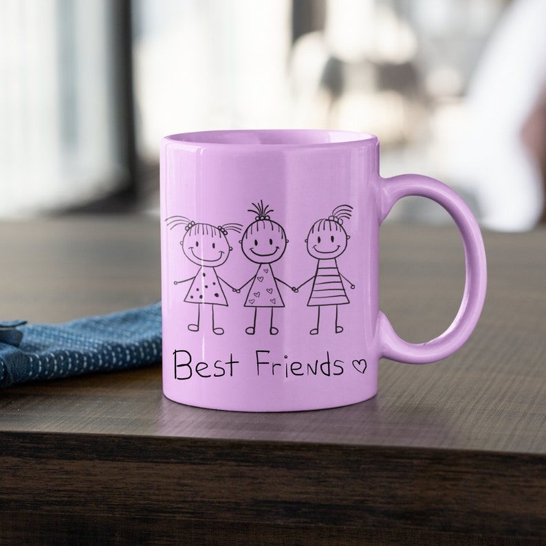 Op de afbeelding: Een lavendelkleurige keramische mok met een zwarte illustratie van drie stokpoppetjes die elkaars hand vasthouden en de tekst "Best Friends" met een hartje.
