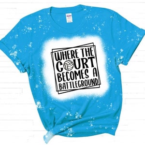 K&ouml;nnte beinhalten: Ein blaues T-Shirt mit wei&szlig;en Bleichmittelspritzern und einer schwarzen Grafik, auf der "Where the court becomes a battleground" mit einer Volleyballgrafik steht.