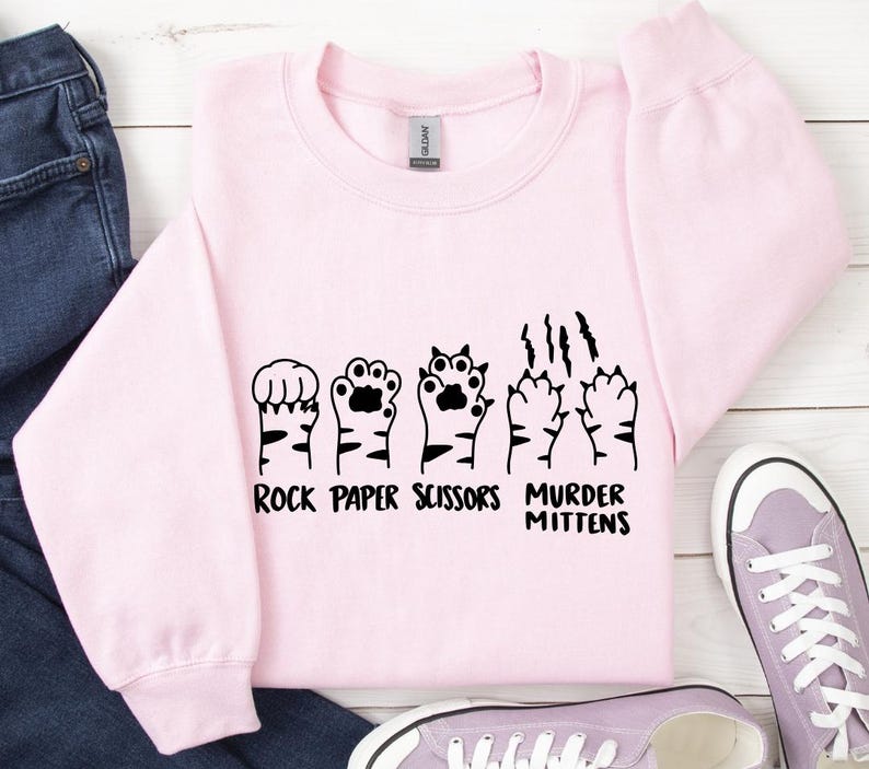 May include: Pink sweatshirt with a black graphic of cat paws and the text "Rock Paper Scissors Murder Mittens".