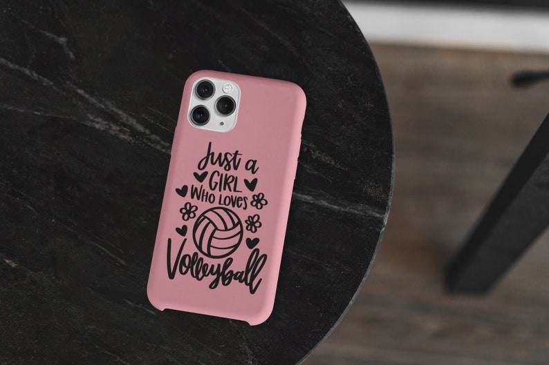 May include: Pink phone case with a black design that says "Just a girl who loves volleyball" with a volleyball graphic.