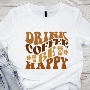 May include: White t-shirt with brown text that reads "Drink Coffee Be Happy" with a coffee cup graphic.