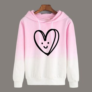 May include: Pink ombre hoodie with a black and white cartoon heart with a smiley face on it.