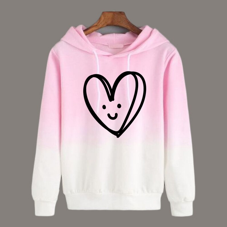 May include: Pink ombre hoodie with a black and white cartoon heart with a smiley face on it.