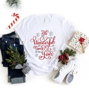May include: White t-shirt with the text "It's the most Wonderful Time of the Year" in red cursive lettering with snowflakes.