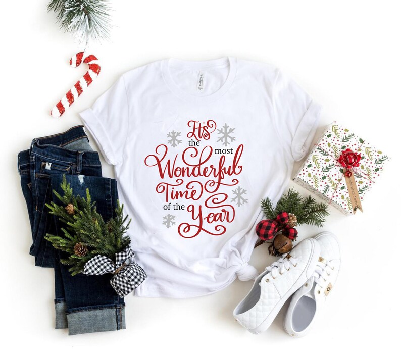 May include: White t-shirt with the text "It's the most Wonderful Time of the Year" in red cursive lettering with snowflakes.