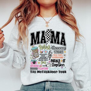 May include: Gray sweatshirt with a graphic print that says "Mama Work Grocery Store" and includes illustrations of a coffee cup, a camera, a heart, and a lightning bolt. The text "The Motherhood Tour" is printed below the graphic.