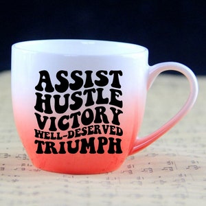 May include: White ceramic mug with a red ombre design. The mug has black text that reads "Assist Hustle Victory Well-Deserved Triumph" in a retro font.