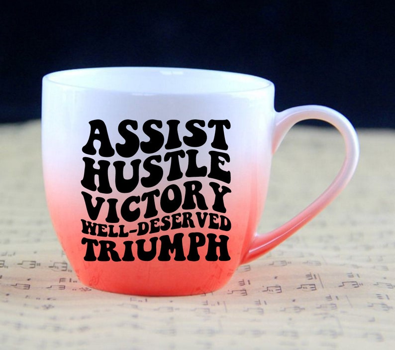 May include: White ceramic mug with a red ombre design. The mug has black text that reads "Assist Hustle Victory Well-Deserved Triumph" in a retro font.