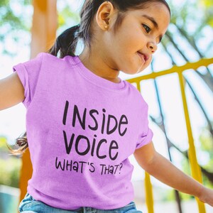 May include: A young person wearing a light purple t-shirt with the text "Inside Voice What's That?" printed on it.