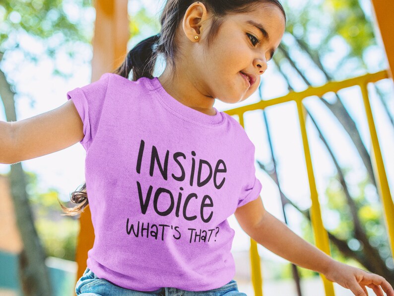 May include: A young person wearing a light purple t-shirt with the text "Inside Voice What's That?" printed on it.