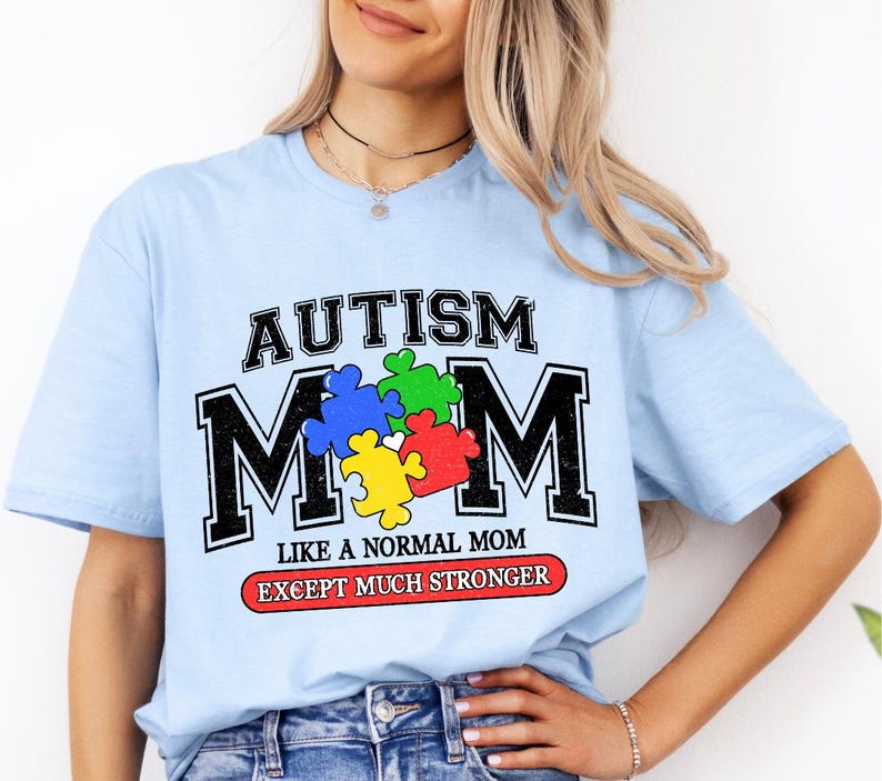 May include: Light blue t-shirt with the text "Autism Mom" in black and white with a colorful puzzle piece design. The text below reads "Like a normal mom except much stronger."