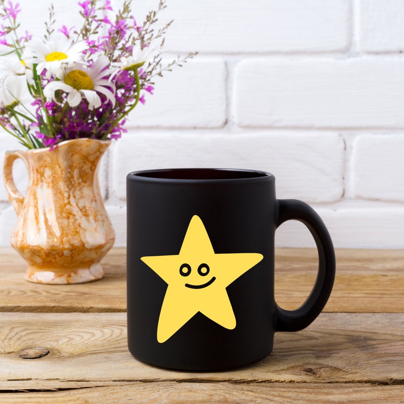 May include: Black coffee mug with a yellow smiling star design. The mug is on a wooden surface.