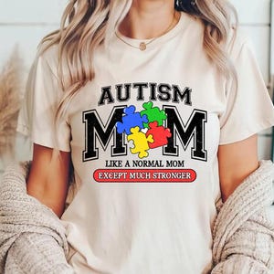 May include: White t-shirt with the text "Autism Mom" in black letters with a puzzle piece design in the middle. The text "Like a normal mom except much stronger" is printed below the design.