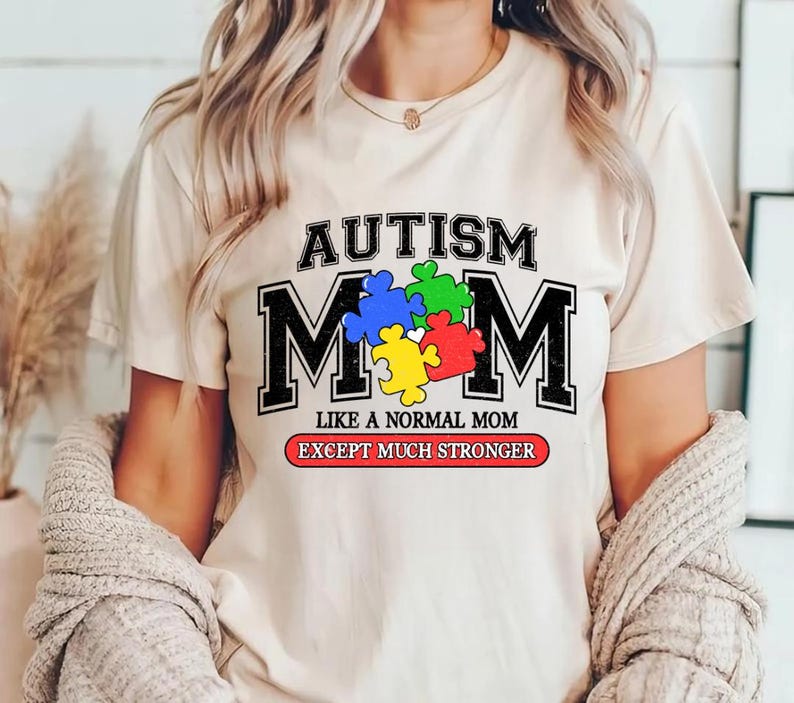 May include: White t-shirt with the text "Autism Mom" in black letters with a puzzle piece design in the middle. The text "Like a normal mom except much stronger" is printed below the design.