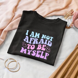 May include: Black t-shirt with the text "I am not afraid to be myself" in pink and blue with smiley faces.
