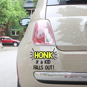 May include: A beige Fiat car with a yellow and black bumper sticker that reads "HONK if a KID FALLS OUT!" The car has a license plate that reads "BFEJ-6" with the word "ONTARIO" above it.