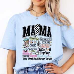 May include: Light blue t-shirt with a graphic print that says "MAMA Work Grocery Store Field Trips Playground Make It Happen Kitchen Practice Sport Games The Motherhood Tour".
