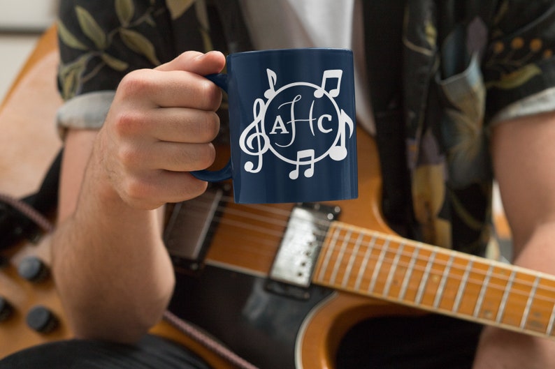 May include: A blue ceramic mug with a white design of musical notes and the letters "AFC" in a circle. The mug is being held by a person wearing a floral shirt.
