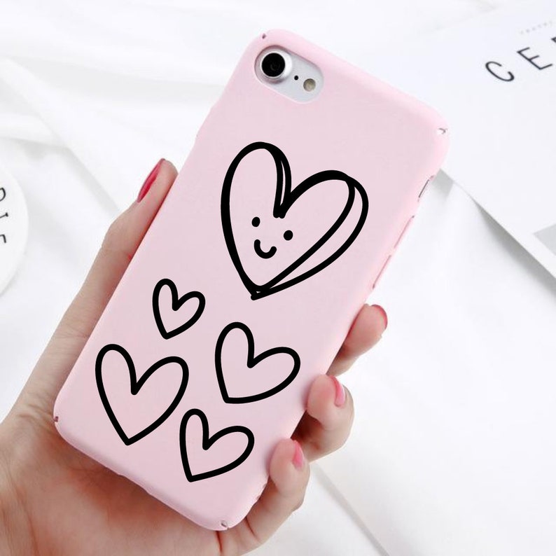 May include: A pink phone case with a black outline of a heart with a smiley face and smaller hearts around it.