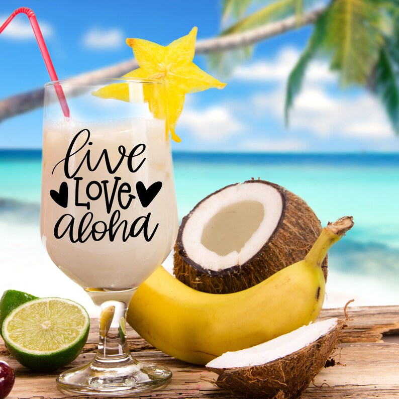 May include: A glass of tropical drink with a straw, a starfruit garnish, and the text "live love aloha" on the side. The drink is on a wooden surface with a coconut, banana, and lime.