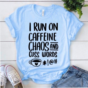 May include: Light blue t-shirt with black text that reads "I run on caffeine chaos and cuss words *!@#" with a coffee cup graphic.