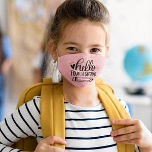 以下が含まれることがあります： ピンクのマスクをつけた若い人が、「hello fourth grade」という文字とハートと鉛筆のデザインをしています。ストライプのシャツと黄色のバックパックを着用しています。