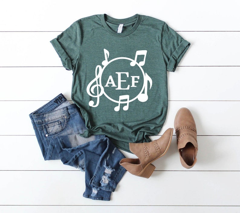 May include: A green t-shirt with a white circle design featuring musical notes and the letters "AEF".