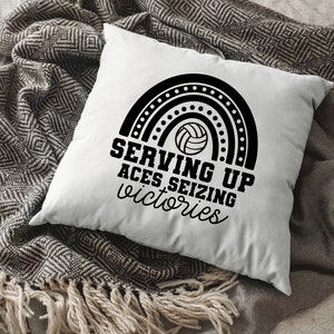 K&ouml;nnte beinhalten: Ein wei&szlig;es Kissen mit schwarzem Text und einer schwarz-wei&szlig;en Volleyballgrafik. Der Text lautet "Serving Up Aces Seizing Victories".