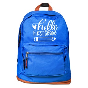 May include: A blue backpack with a brown trim and a white design that says "hello first grade" with a heart and a pencil.