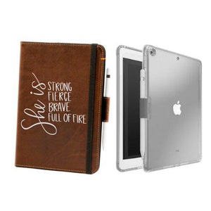 May include: A brown leather iPad case with a white inscription that reads "She is strong fierce brave full of fire". The case is closed and has a black elastic band to hold it closed. A clear plastic iPad case is also shown in the image.
