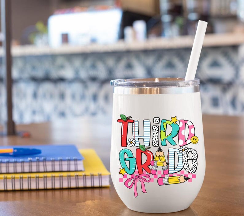 Puede incluir: Un vaso de vino de acero inoxidable blanco con un gr&aacute;fico colorido que dice "Tercer Grado". El gr&aacute;fico incluye una manzana roja, un globo terr&aacute;queo azul, un lazo rosa y l&aacute;pices amarillos.