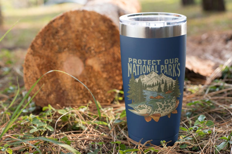May include: Navy blue insulated tumbler with a silver rim, featuring the text "Protect Our National Parks" and a graphic of a mountain scene and a fish. The tumbler is cylindrical and appears to be made of stainless steel.