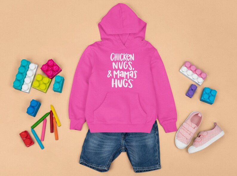May include: Pink hooded sweatshirt with the text "Chicken Nugs, & Mamas Hugs" in white. The sweatshirt is paired with blue denim shorts and pink sneakers.