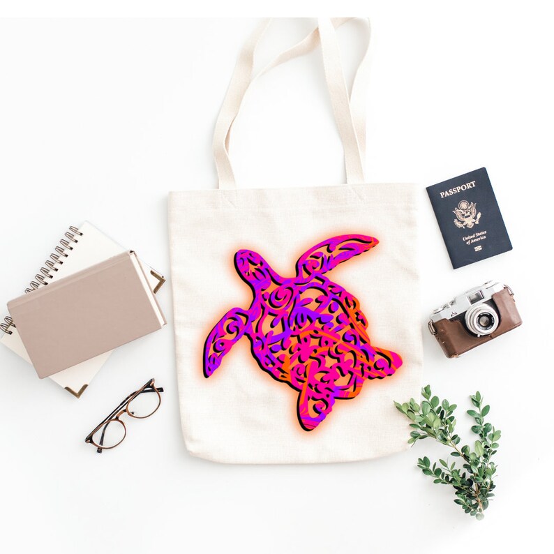 K&ouml;nnte beinhalten: Eine wei&szlig;e Einkaufstasche mit einem pinkfarbenen und orangenfarbenen Muster einer Meeresschildkr&ouml;te. Die Tasche hat lange Henkel und ist aus Canvas.