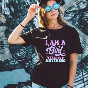 May include: A black t-shirt with a pink and purple graphic that says "I am a girl and I can do anything" with stars and hearts around the text.