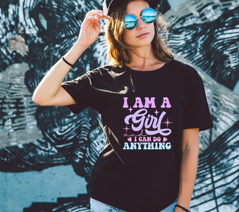 May include: A black t-shirt with a pink and purple graphic that says "I am a girl and I can do anything" with stars and hearts around the text.