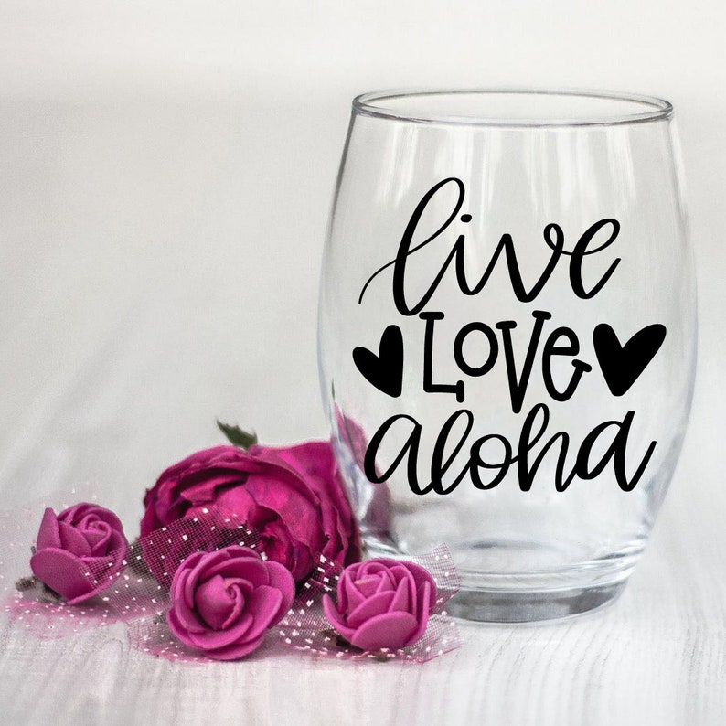 May include: Clear glass wine glass with the text "live love aloha" in black lettering with two small hearts on either side of the word "love".